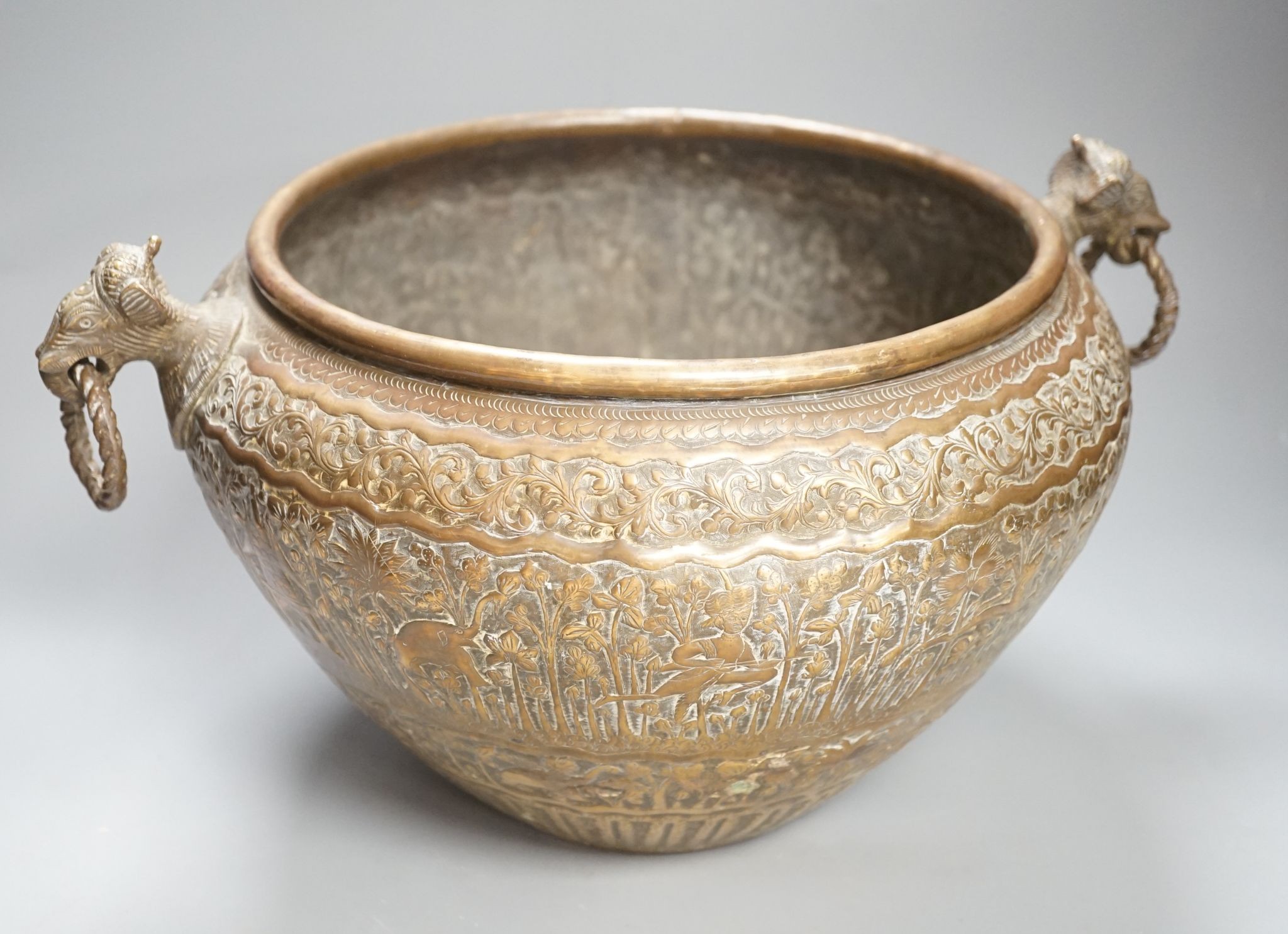 19th century hand engraved British Indian brass jardinière planter vase, finely engraved depicting scenes in an Indian forest with game hunting and elephants; with elephant head handles; original patina.